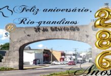 Parabéns Rio-grandinos 286 Anos Pórtico de rio grande dizendo Feliz aniversário Rio grande, com uma silhueta de uma cuia de chimarrão e 3 balões dourados formando o numero 286