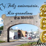 Imagem do pórtico de Rio Grande com o numero 286 em balões dourados e a frase Feliz aniversário. No fundo céu azul e alguns veículos