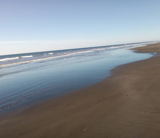 Praia do Cassino Orla do mar. À esquerda o oceano e a esquerda areia da praia. Céu azul sem nuvens
