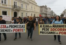 Moradores da Ilha dos Marinheiros Protestam por Reconstrução de Ponte e Prefeitura Reitera Abertura ao Diálogo Manifestação em uma rua do centro histórico de Rio Grande, em frente ao prédio da Prefeitura Municipal. Um grupo de pessoas segura faixas grandes e coloridas exigindo a reconstrução da ponte que liga a Ilha dos Marinheiros ao continente. As faixas dizem: “Basta de promessas. Queremos a ponte!” e “A Ilha dos Marinheiros pede socorro! Precisamos da ponte”. Ao fundo, observa-se a arquitetura clássica de prédios antigos, com colunas brancas e detalhes em amarelo, além de várias pessoas participando do protesto, demonstrando preocupação e engajamento com a causa. O céu está nublado, e o ambiente é pacífico, porém carregado de indignação