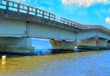 Monitoramento das obras na ponte da Ilha dos Marinheiros Foto da ponte que liga a Ilha dos Marinheiros ao continente. Céu azul com nuvens, gaivotas e agua escura da lagoa, compõem a imagem juto à ponte branca e rebaixada no centro, mostrando que está quebrando.